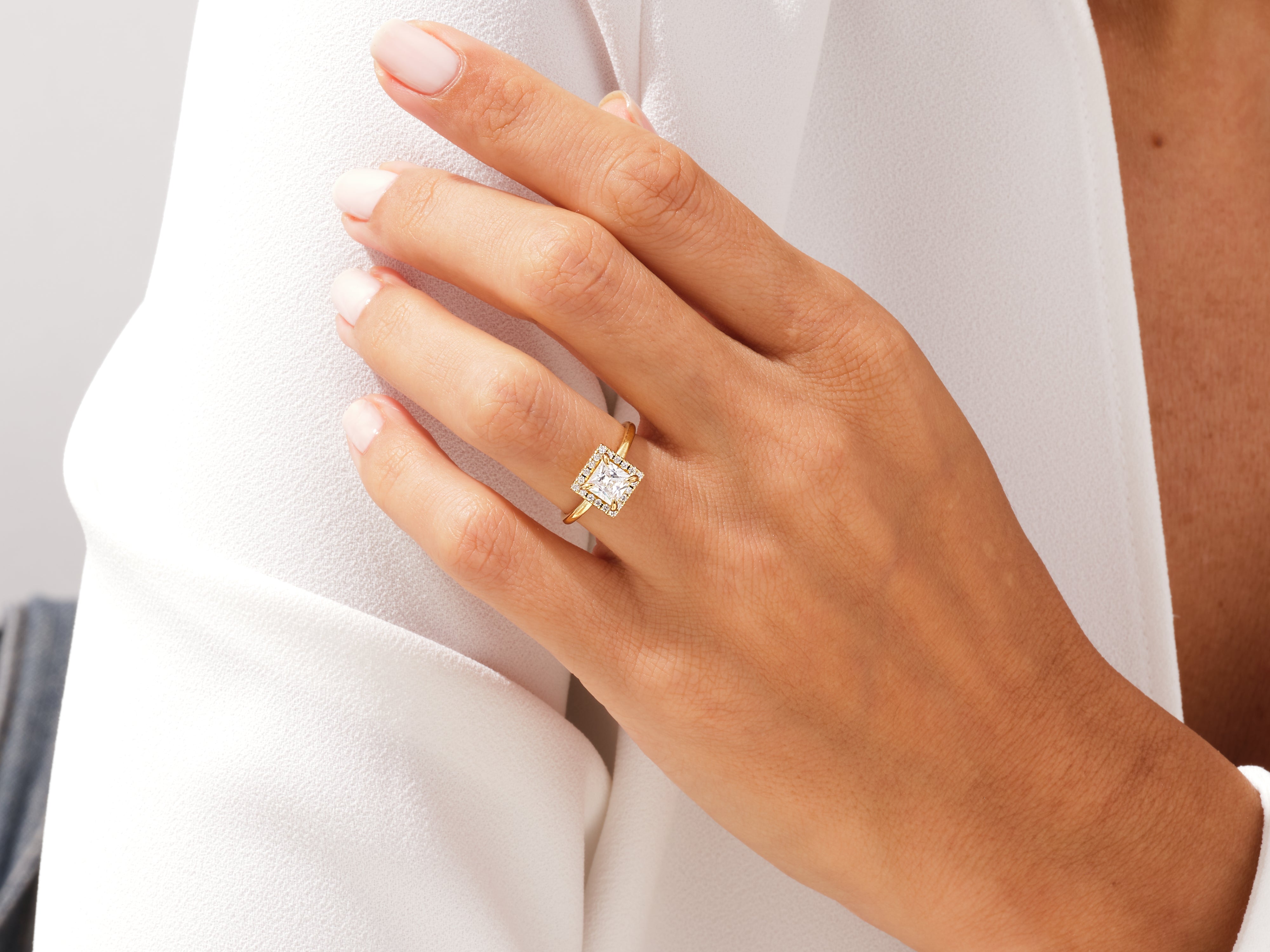 Gold princess cut diamond halo engagement ring on hand
