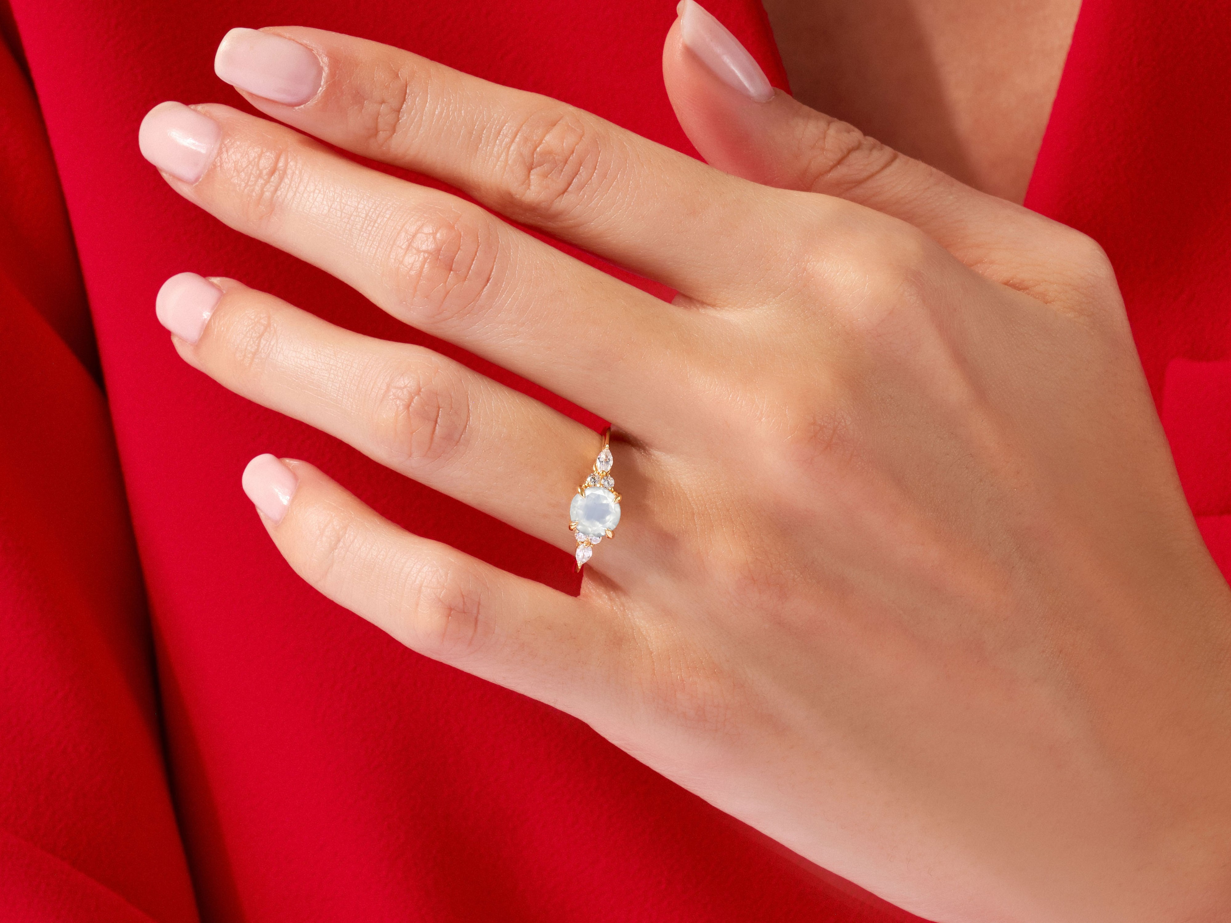 Gold ring with oval moonstone and diamonds on a red background