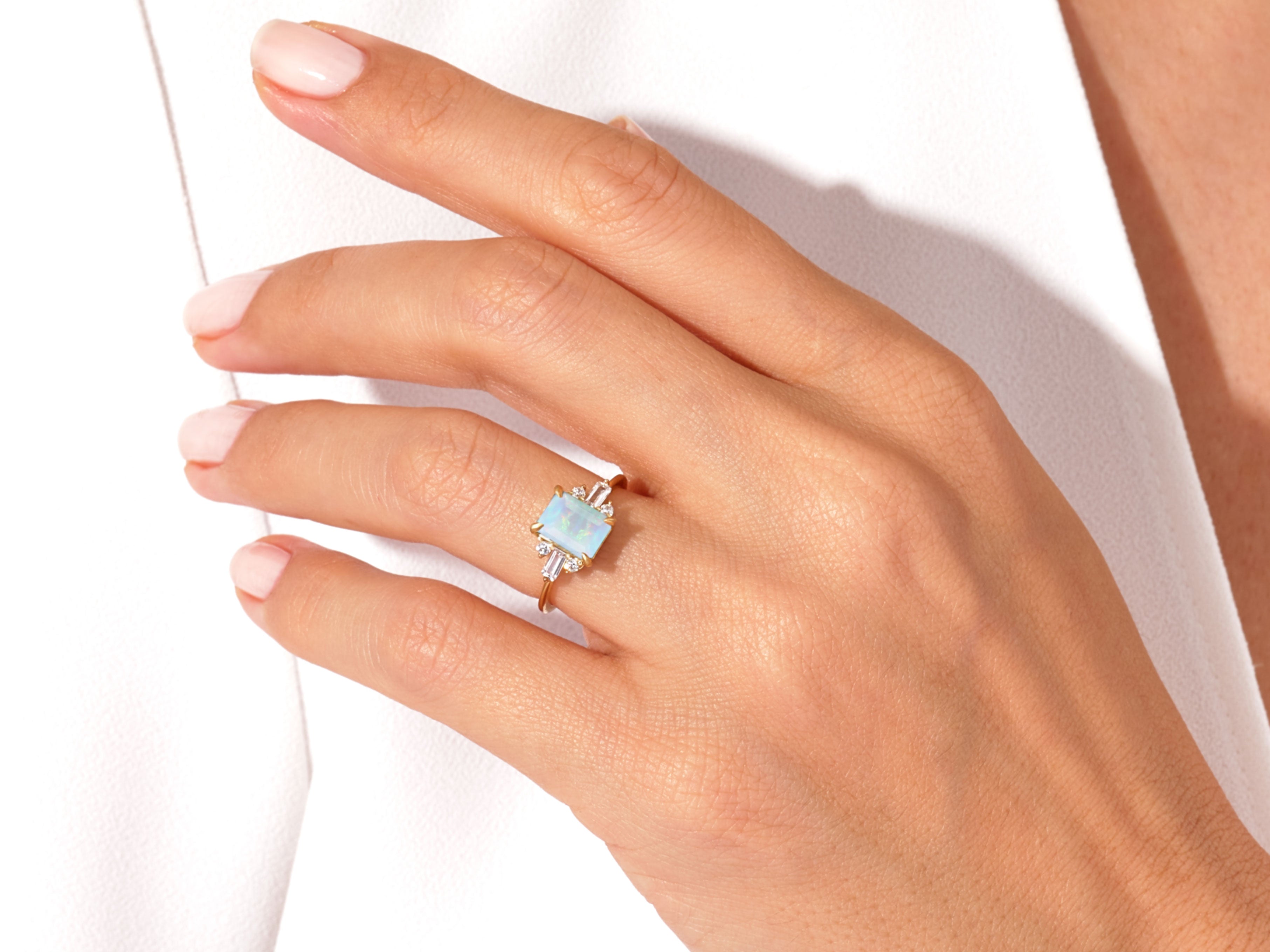 Emerald cut opal ring with diamond accents on a hand