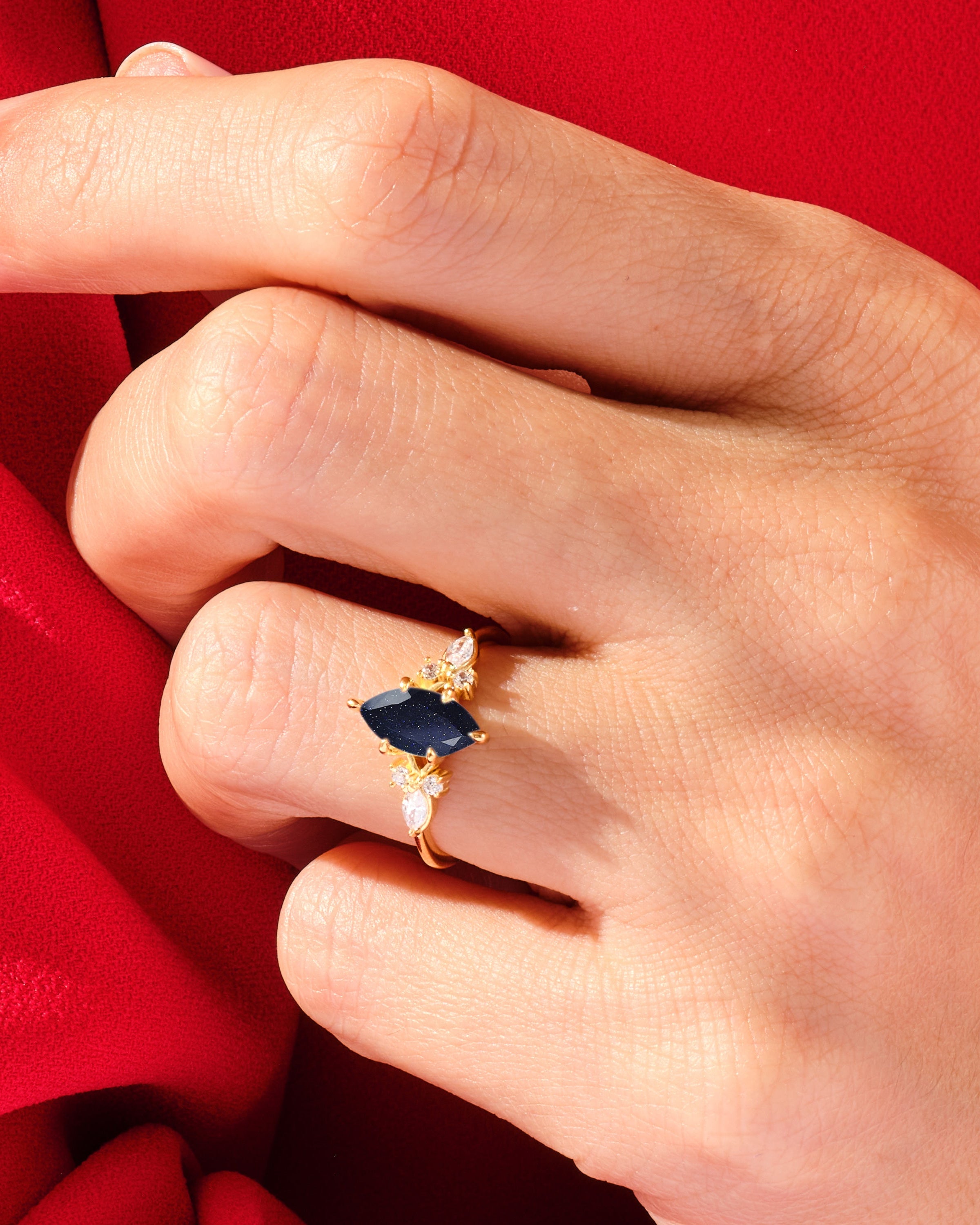 Gold ring with dark blue marquise gemstone and diamonds on red fabric