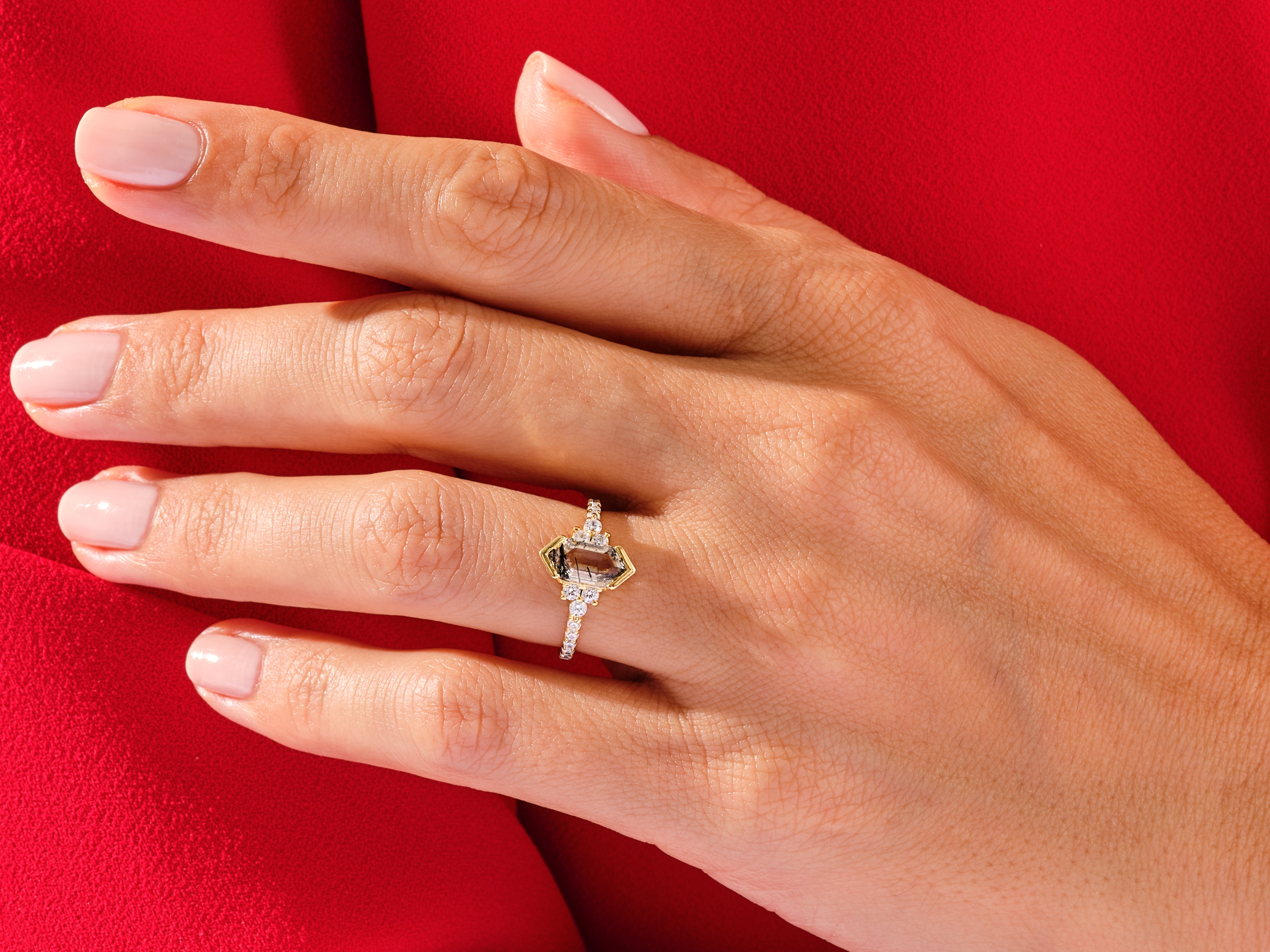 Emerald cut gemstone ring with diamonds on a red background