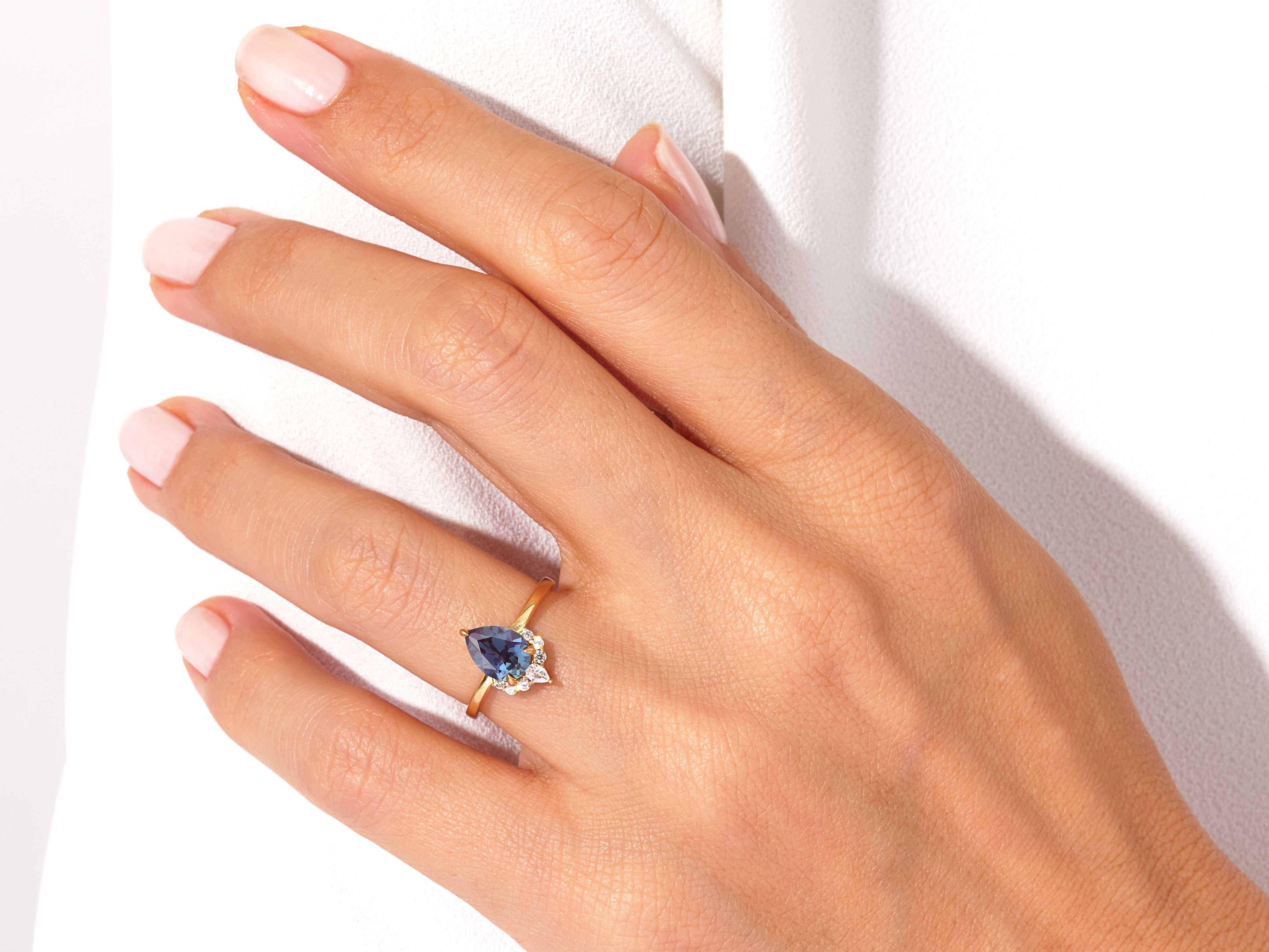 Gold pear-shaped sapphire ring with diamond accents on hand