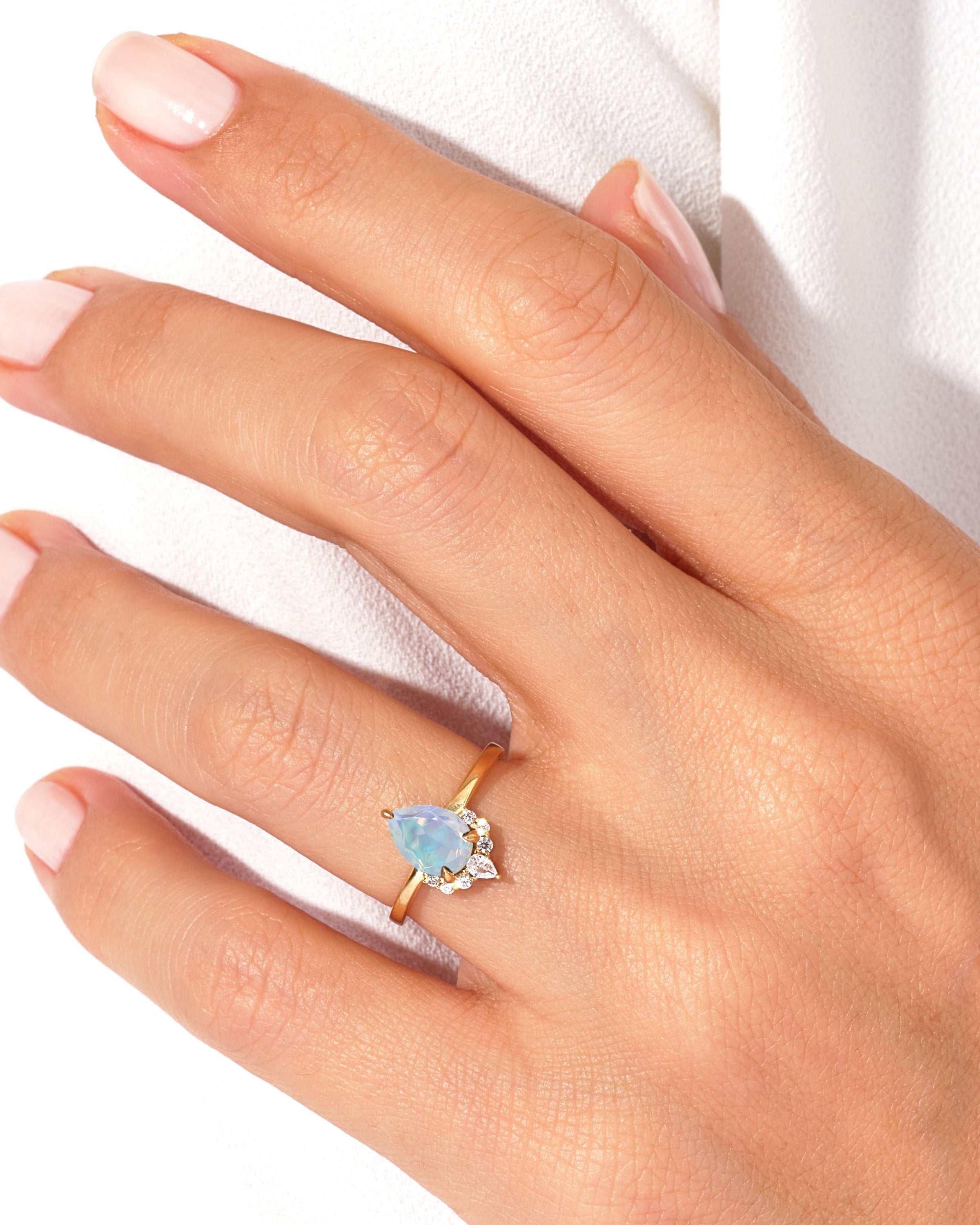 Gold ring with pear-shaped opal and diamond accents on a hand