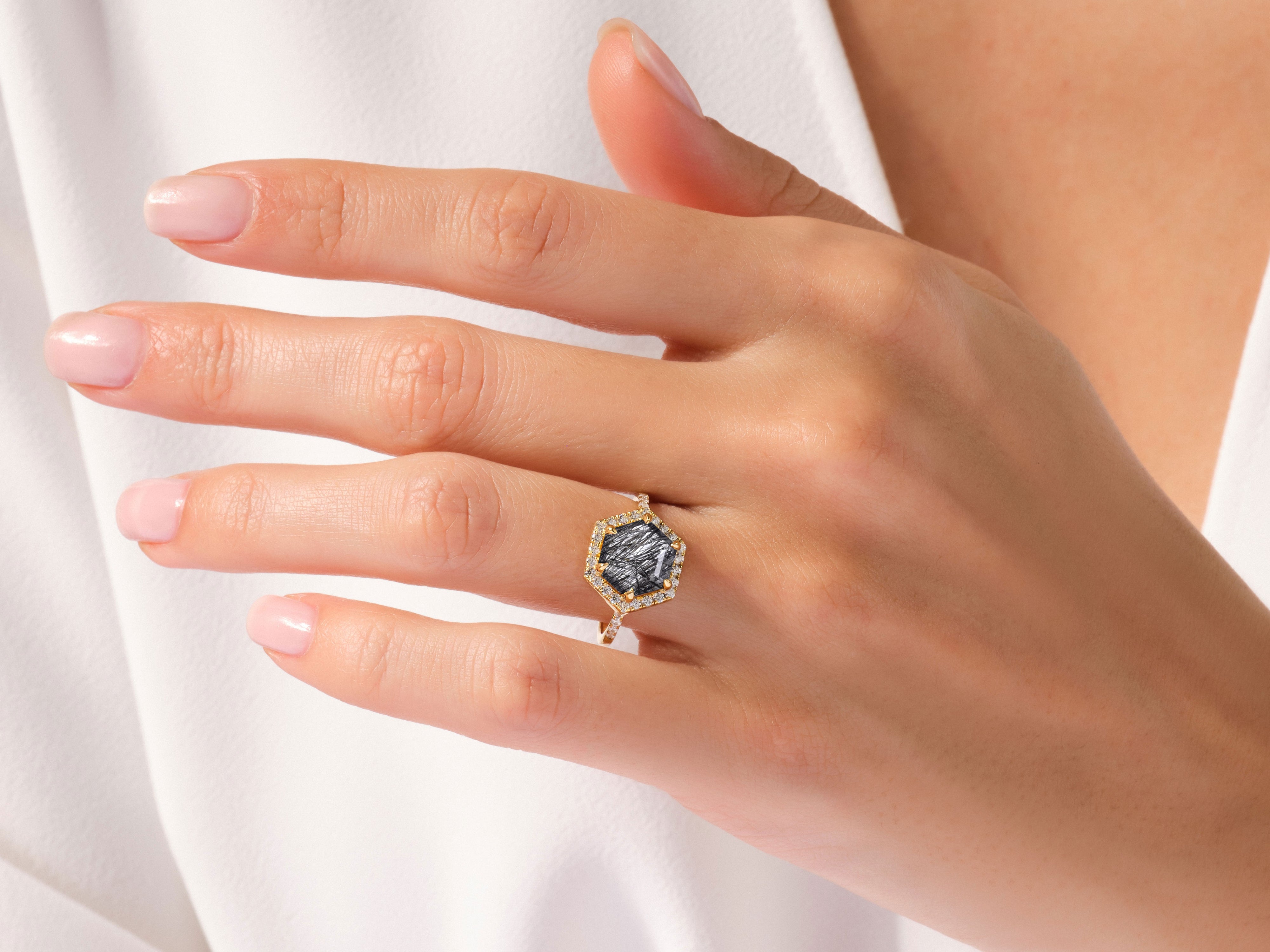 Hexagonal gemstone ring with diamond halo on a woman's hand