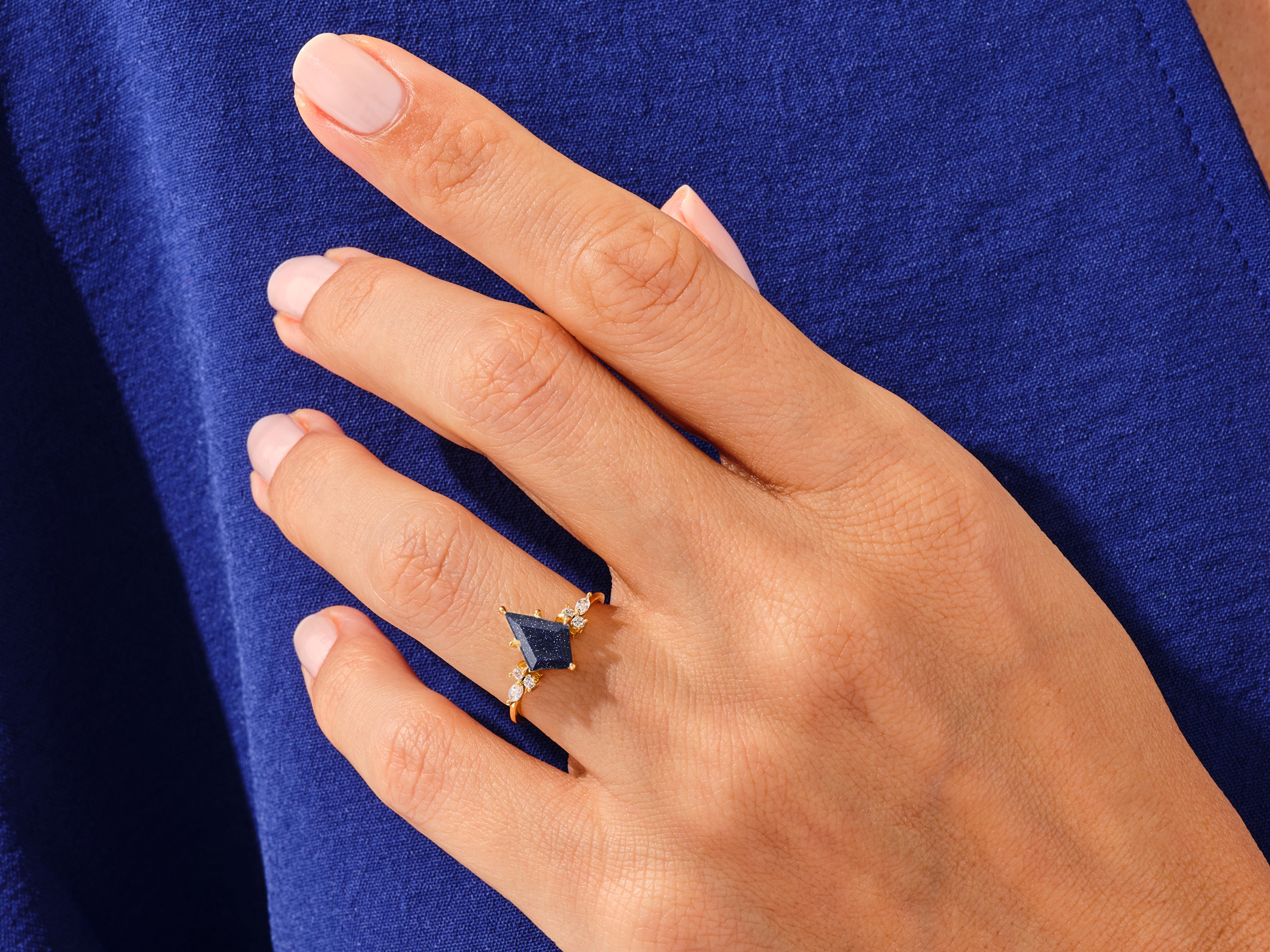 Gold ring with dark blue gemstone and diamonds on hand