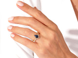 Gold ring with dark blue stone and diamonds on a hand