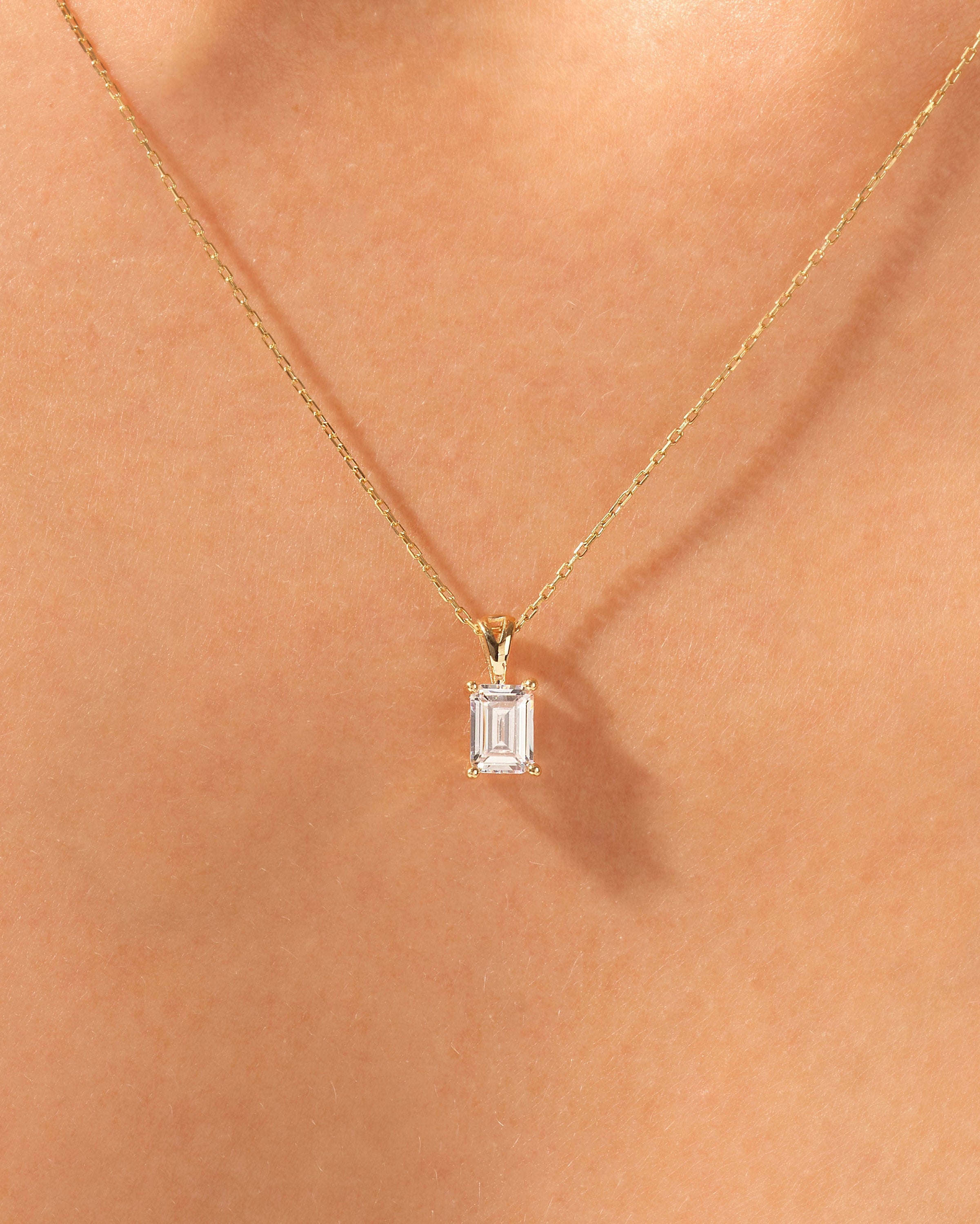 Gold necklace with emerald cut diamond pendant on skin